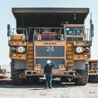 A man standing in front of a large yellow mining dump truck