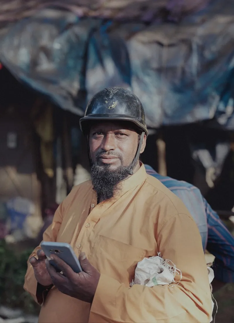 A bearded worker in a hard hat and work shirt holding a tablet on site