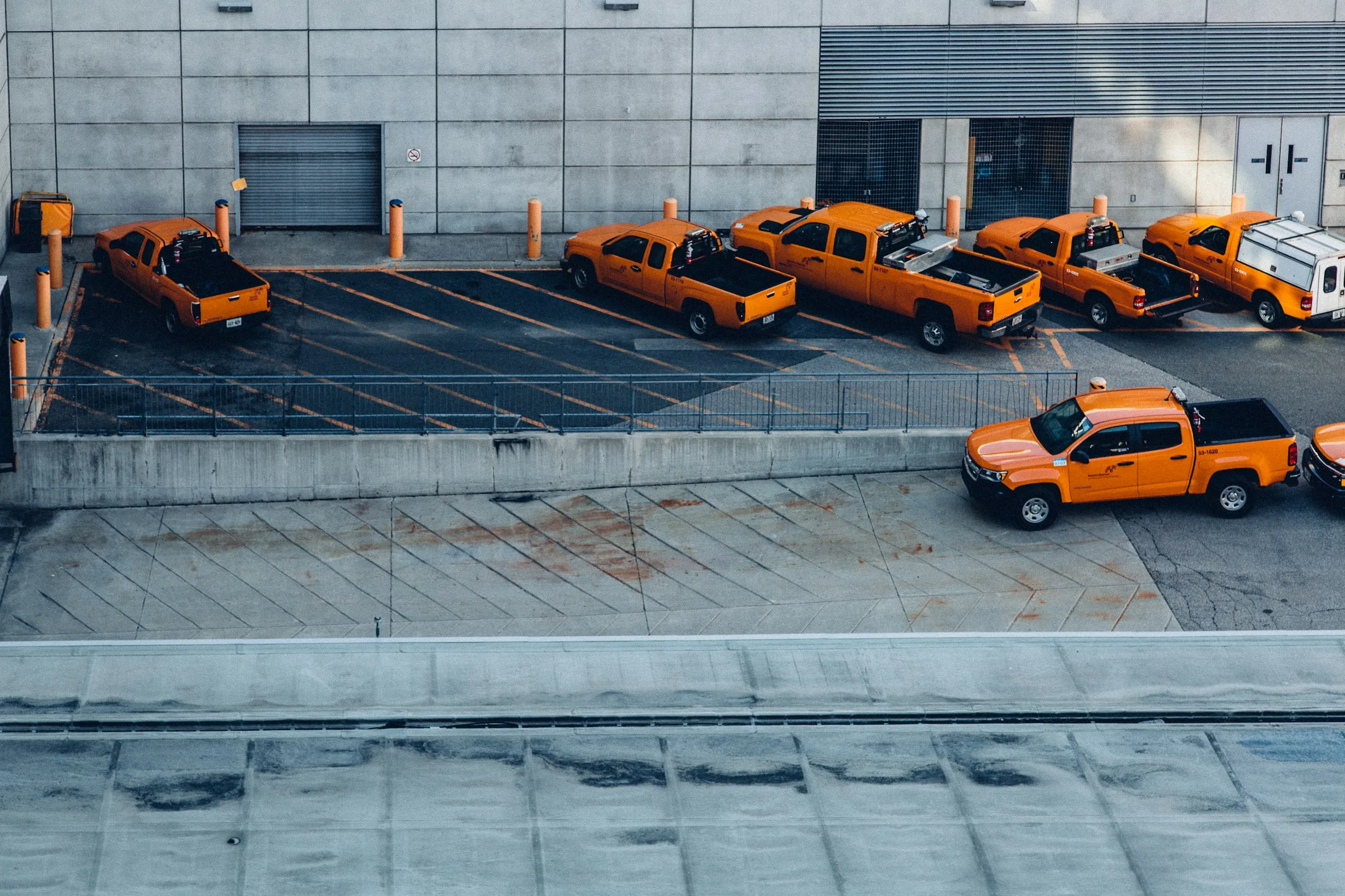 A fleet of orange pickup trucks parked in a row at an operations yard.