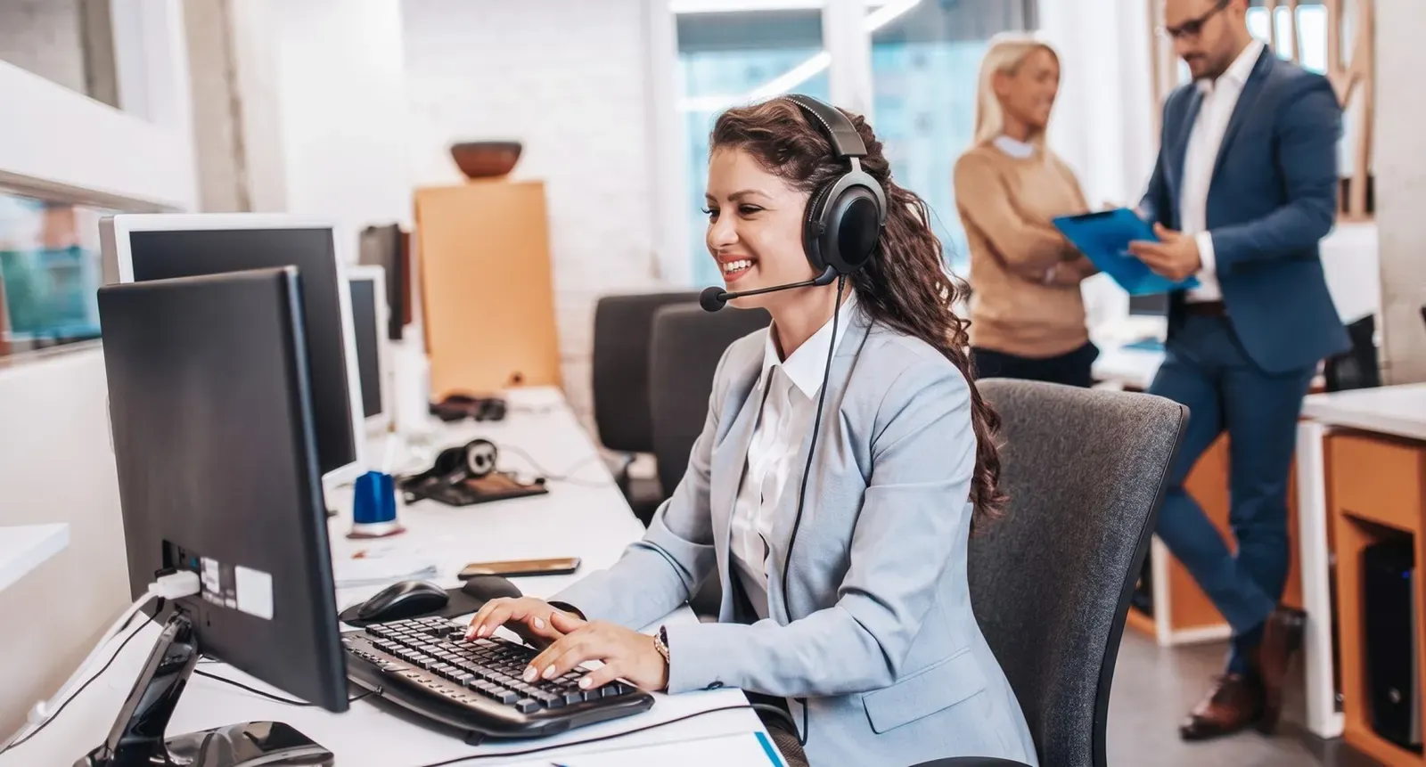 Helpdesk agent wearing a headset and typing at a computer in a busy office