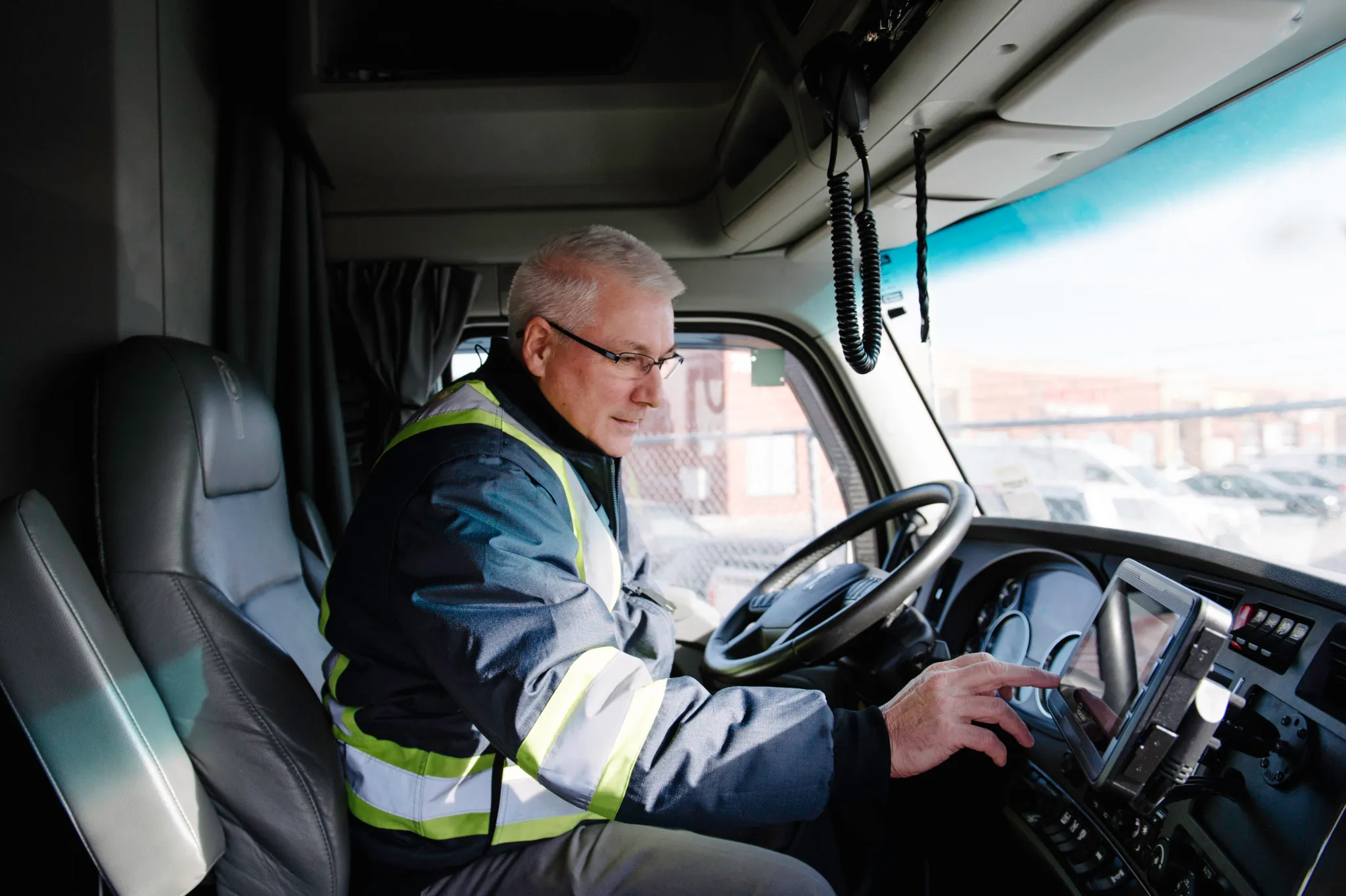 Driver in a reflective safety jacket using a touchscreen device inside a truck cab
