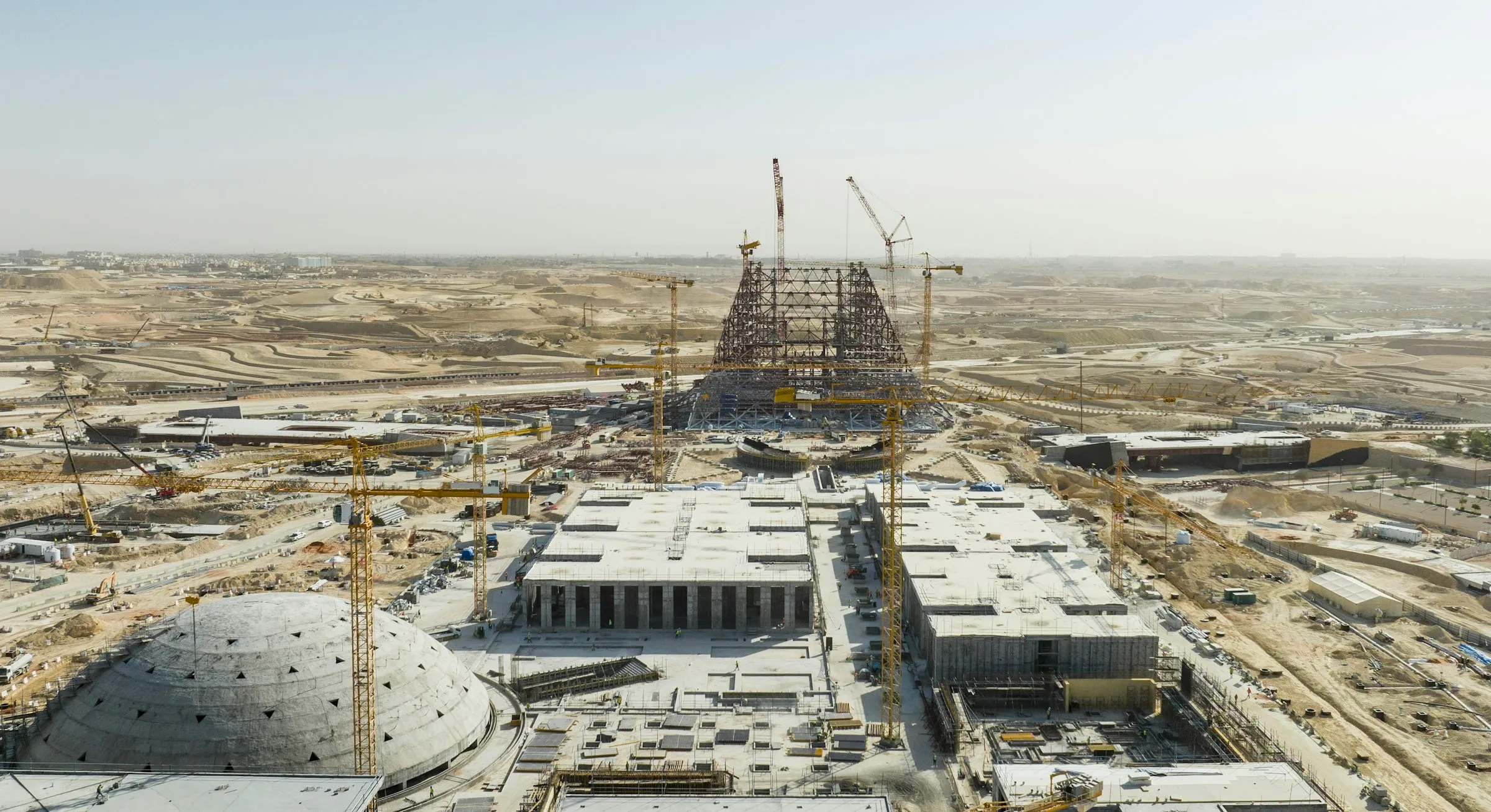 Aerial view of a large construction site in the desert near Riyadh, with tower cranes and concrete structures.