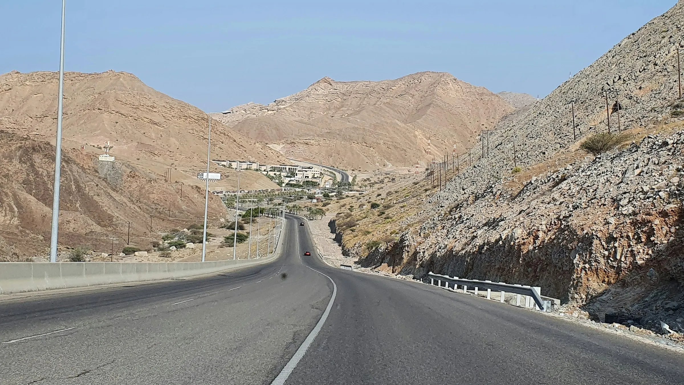 A long road winds between dry brown mountains near Muscat, Oman.