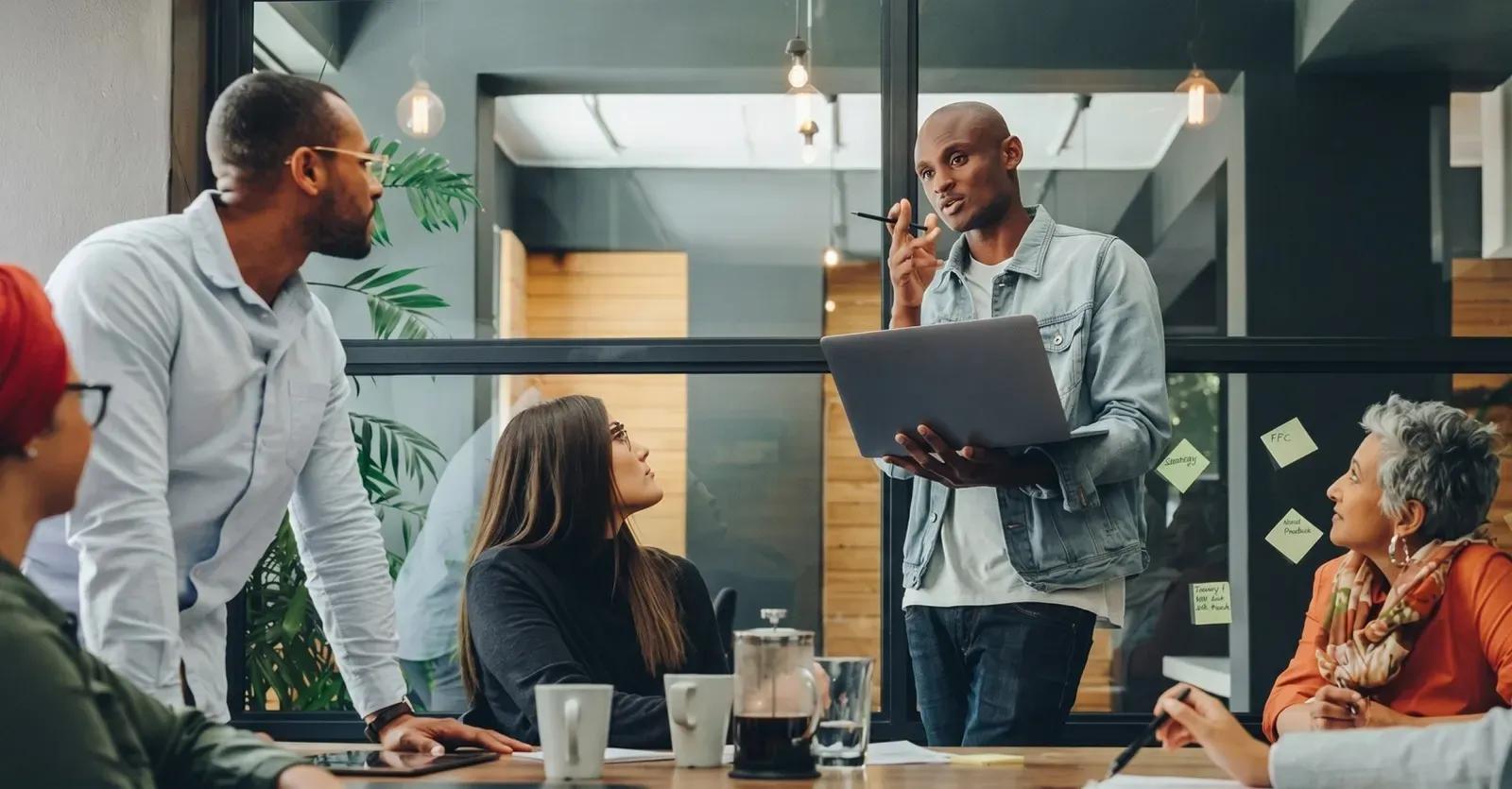 Colleague standing with a laptop, presenting to a team seated around a meeting table