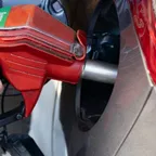 A hand holding a red fuel nozzle inserted into a vehicle's fuel filler.