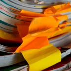 A tall, messy stack of paper notebooks and files with crumpled orange and yellow handwritten sticky notes poking out.