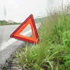A red and orange warning triangle set up on the roadside verge beside a road.