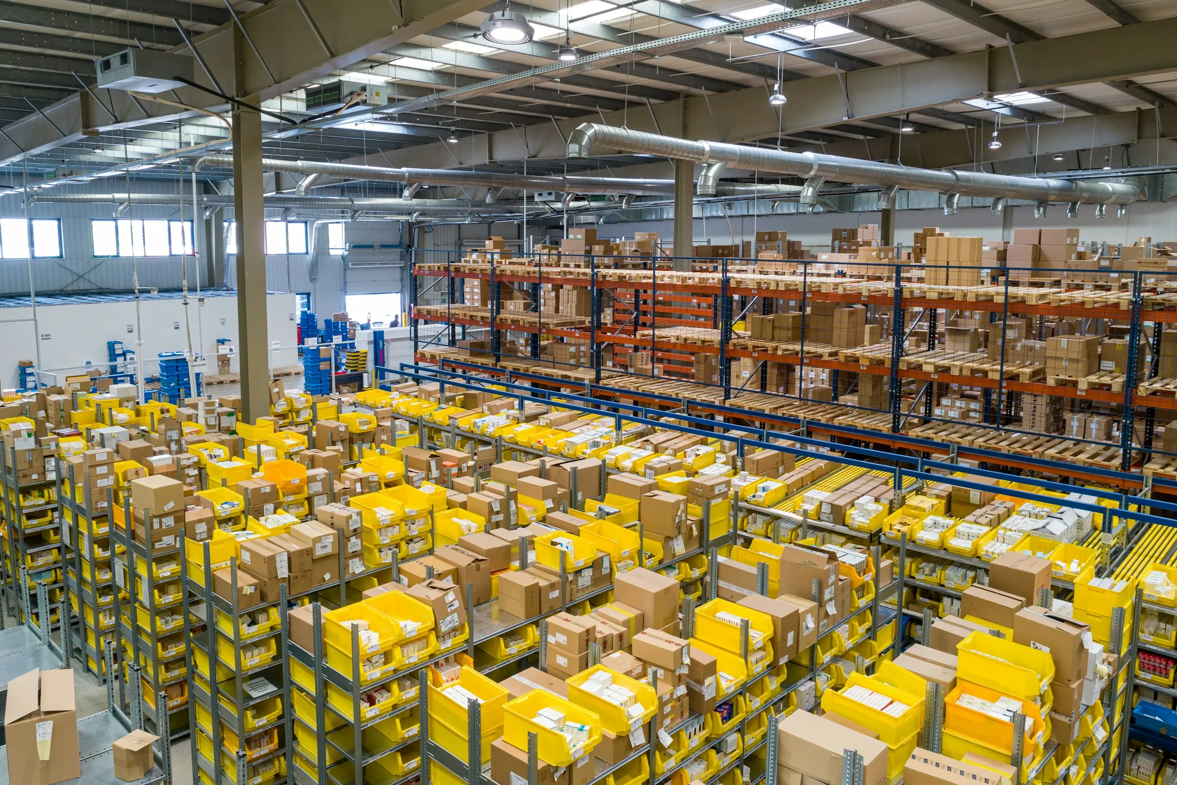 High view of a warehouse with rows of shelving full of yellow storage bins and cardboard boxes.