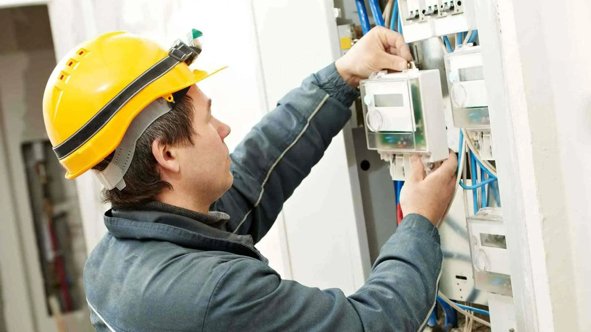 Technician in a hard hat installing an electricity meter in a distribution panel